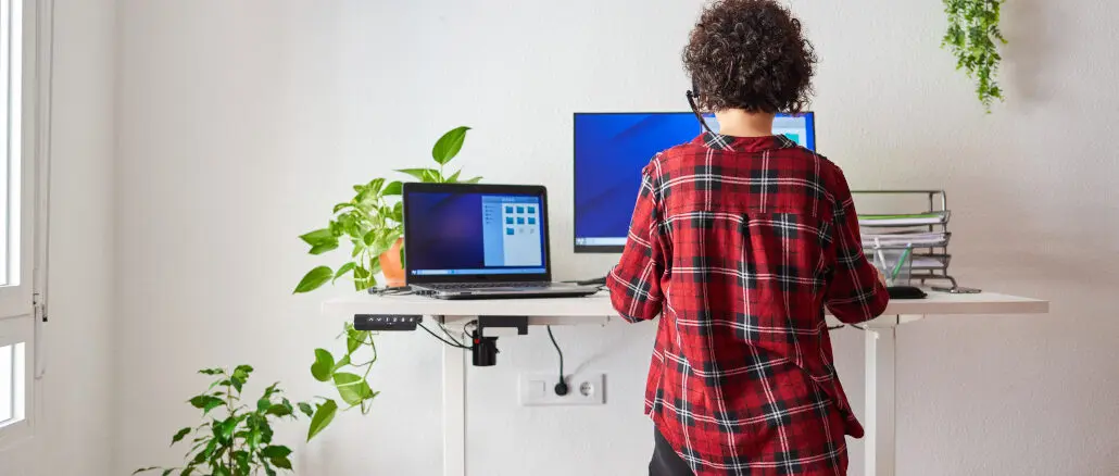 Eine Frau arbeitet am Laptop an einem höhenverstellbaren Schreibtisch
